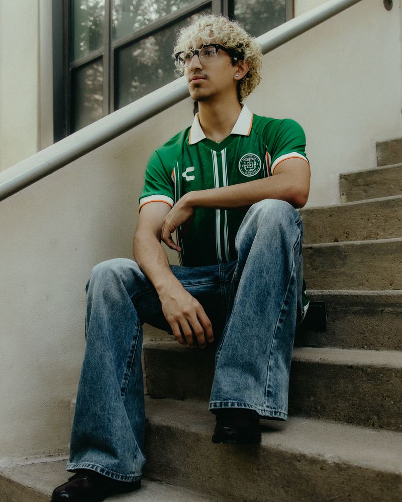 Model in a green Charly Orgullo México jersey and wide-leg jeans sitting on outdoor stairs