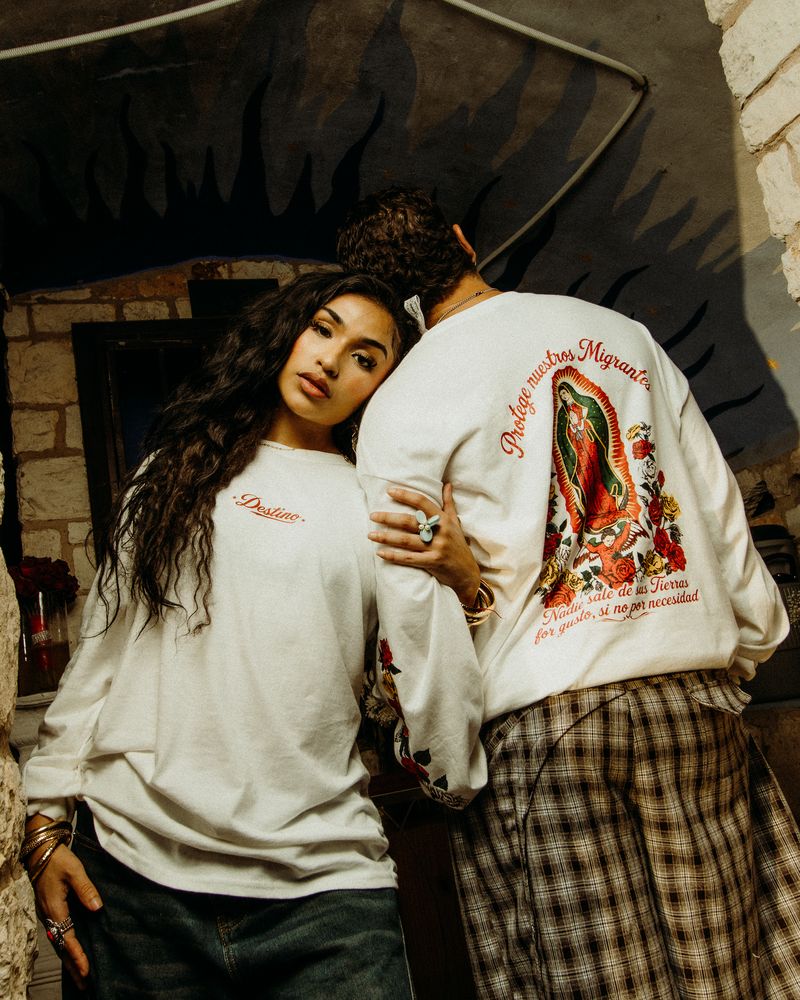 Two models in cream Destino long-sleeve graphic tees against a painted stone wall